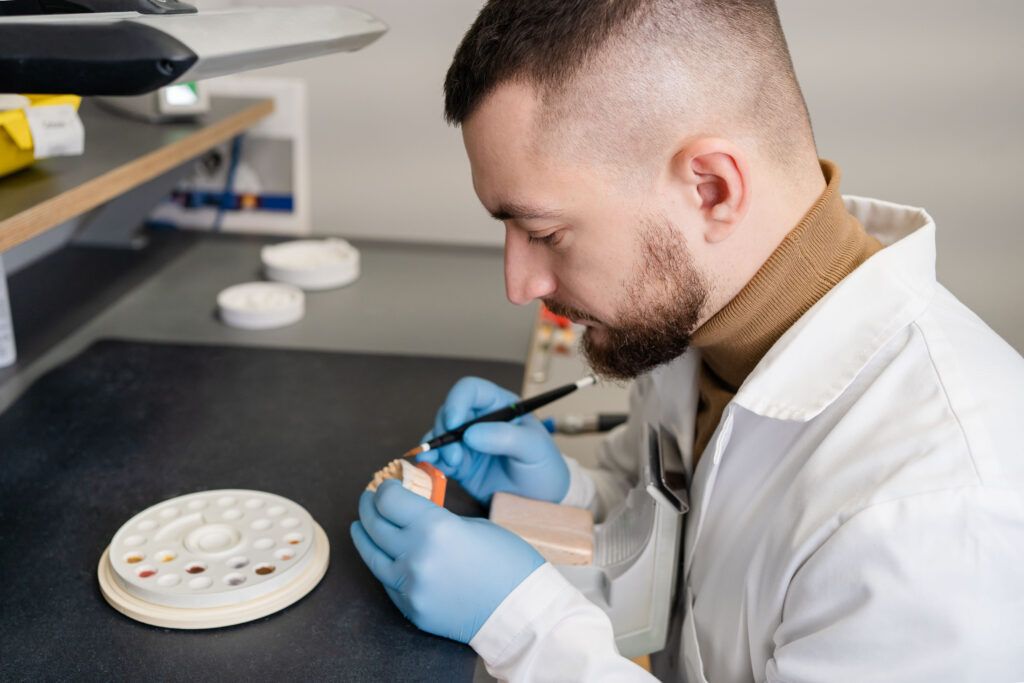 Dental technician using a brush with ceramic dental implants in his laboratory.