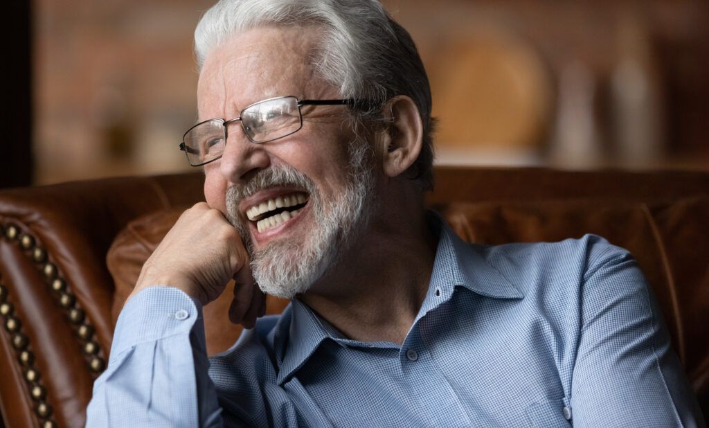 Mature man sit on sofa laugh demonstrate healthy straight teeth