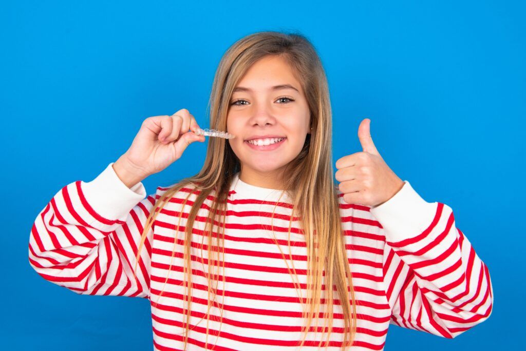 MODEL holding an invisible braces aligner and rising thumb up, recommending this new treatment. Dental healthcare concept.